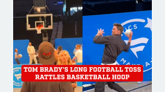 Tom Brady shakes the hoop as he throws the football from the other end of the basketball court