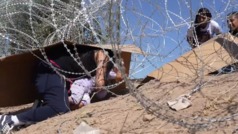Mujer con su hija pequeña intenta pasar bajo cerca con púas en frontera de México con El Paso, Texas